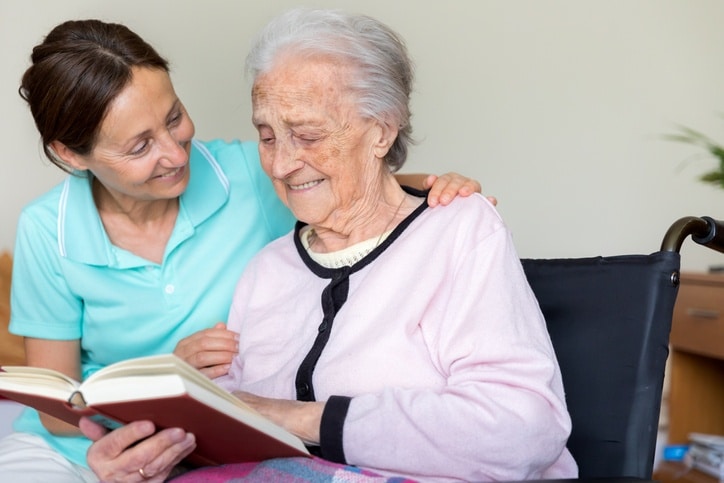 Caregiver reading a book with a senior woman in dementia care