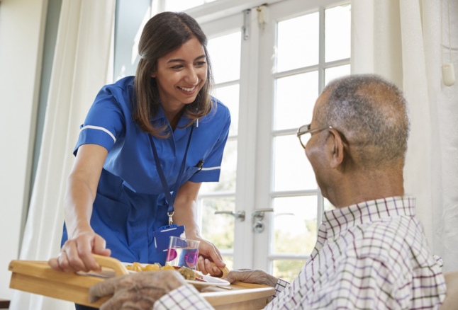 Skilled nurse serving dinner to a senior man at a nursing facility in Shreveport, LA