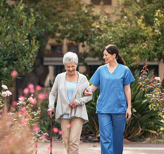 Nurse and senior woman stroll courtyard during a respite stay at a Shreveport nursing facility